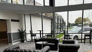 A spacious indoor area with large windows, black leather sofas, and a ceiling fan. - Britannia Hotel Wigan (Wigan)