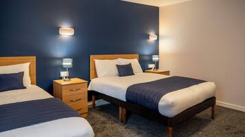 A hotel room with two beds, wooden headboards, bedside tables, and wall-mounted lamps.