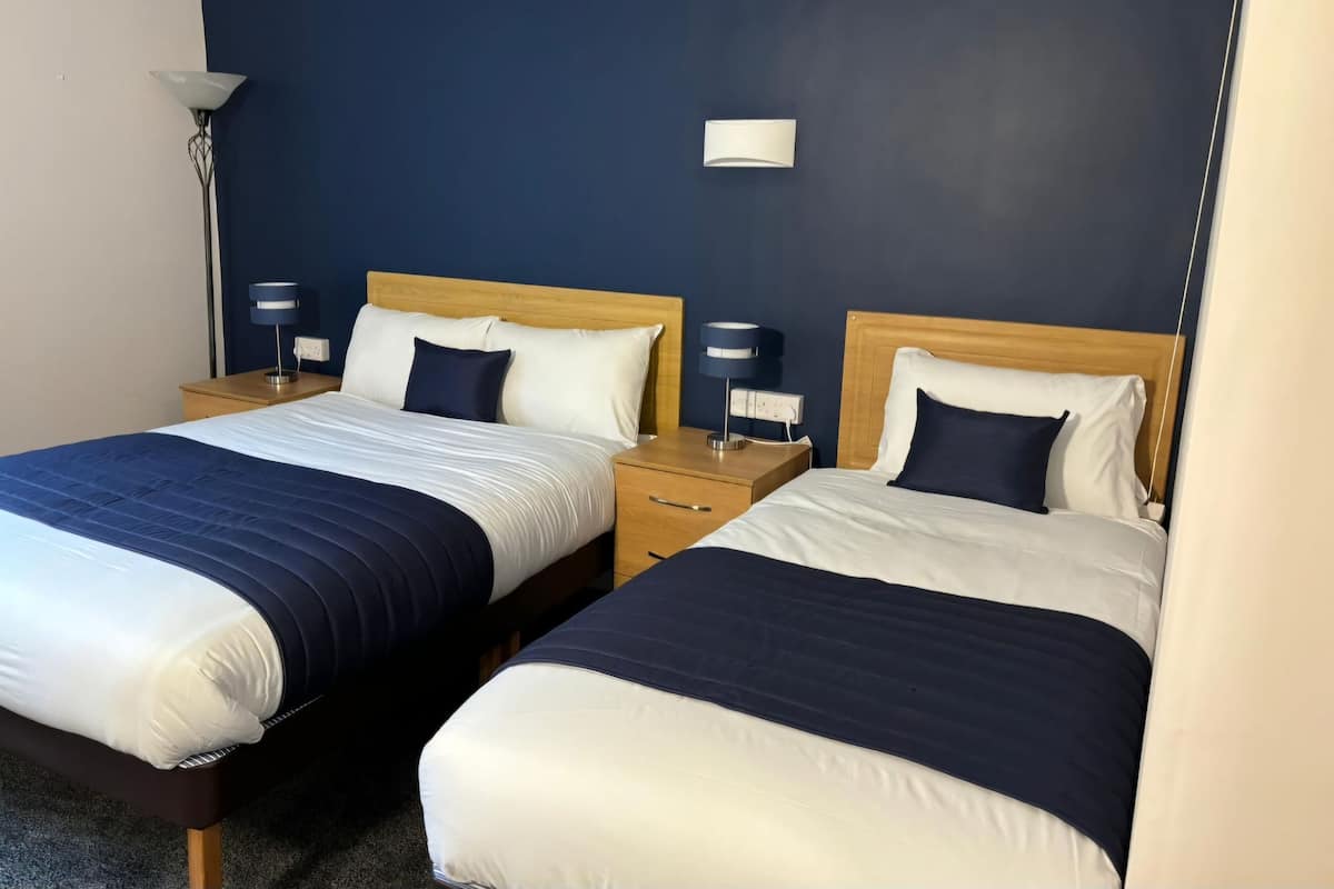 A hotel room with two beds, each with a wooden headboard, white and navy bedding, and bedside lamps.