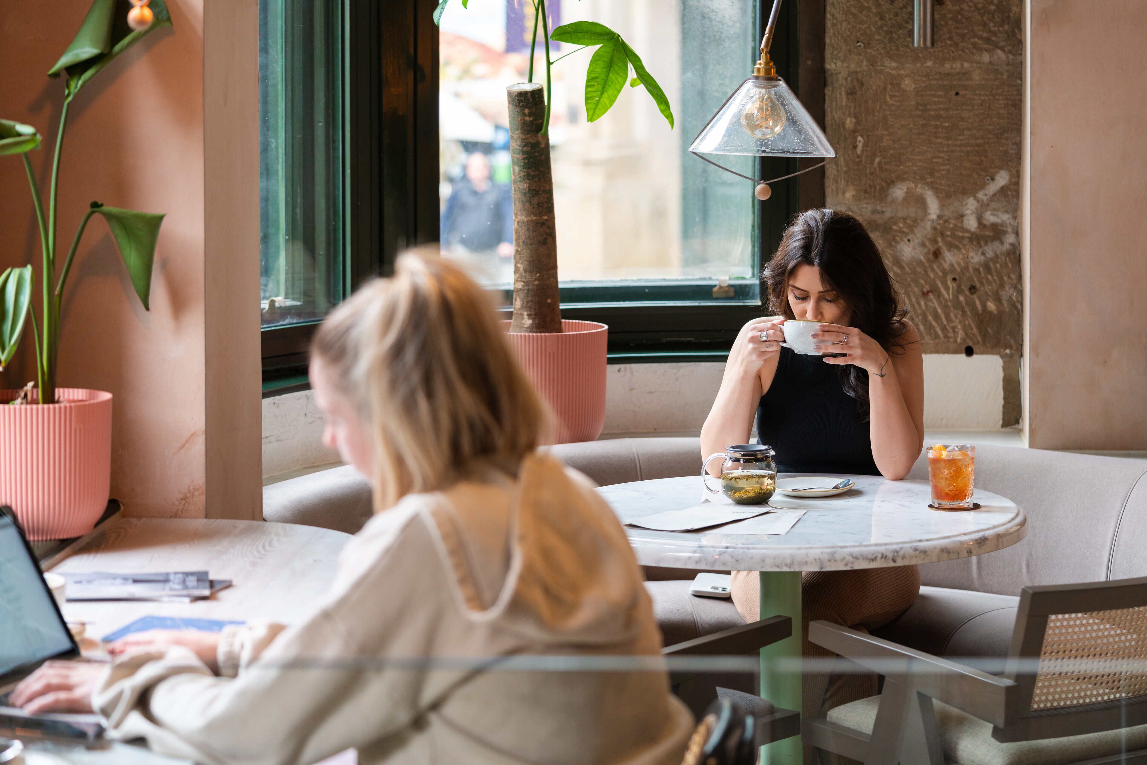 A cafe with round tables, a laptop on one table, and a potted plant on the other.