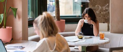 Un café con mesas redondas, un ordenador portátil sobre una y una planta en maceta sobre la otra.