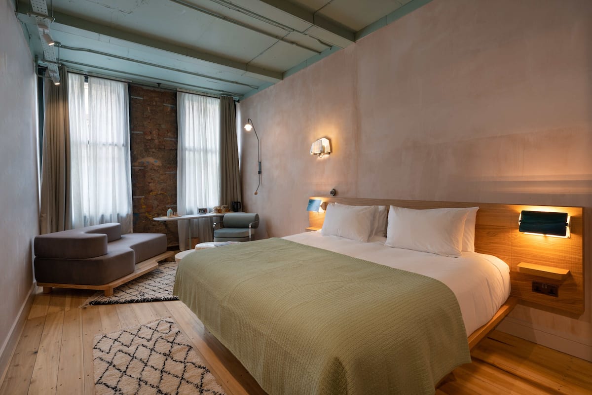 A modern bedroom with a large bed, a wooden headboard, a nightstand, a lamp, and a seating area with a chair and a small table.