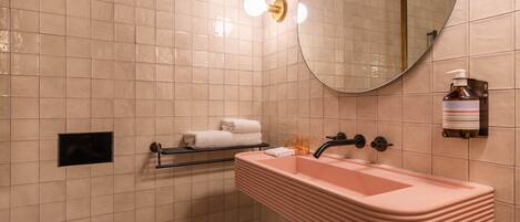 Un baño con un lavamanos rosa, un espejo y un perchero para toallas.