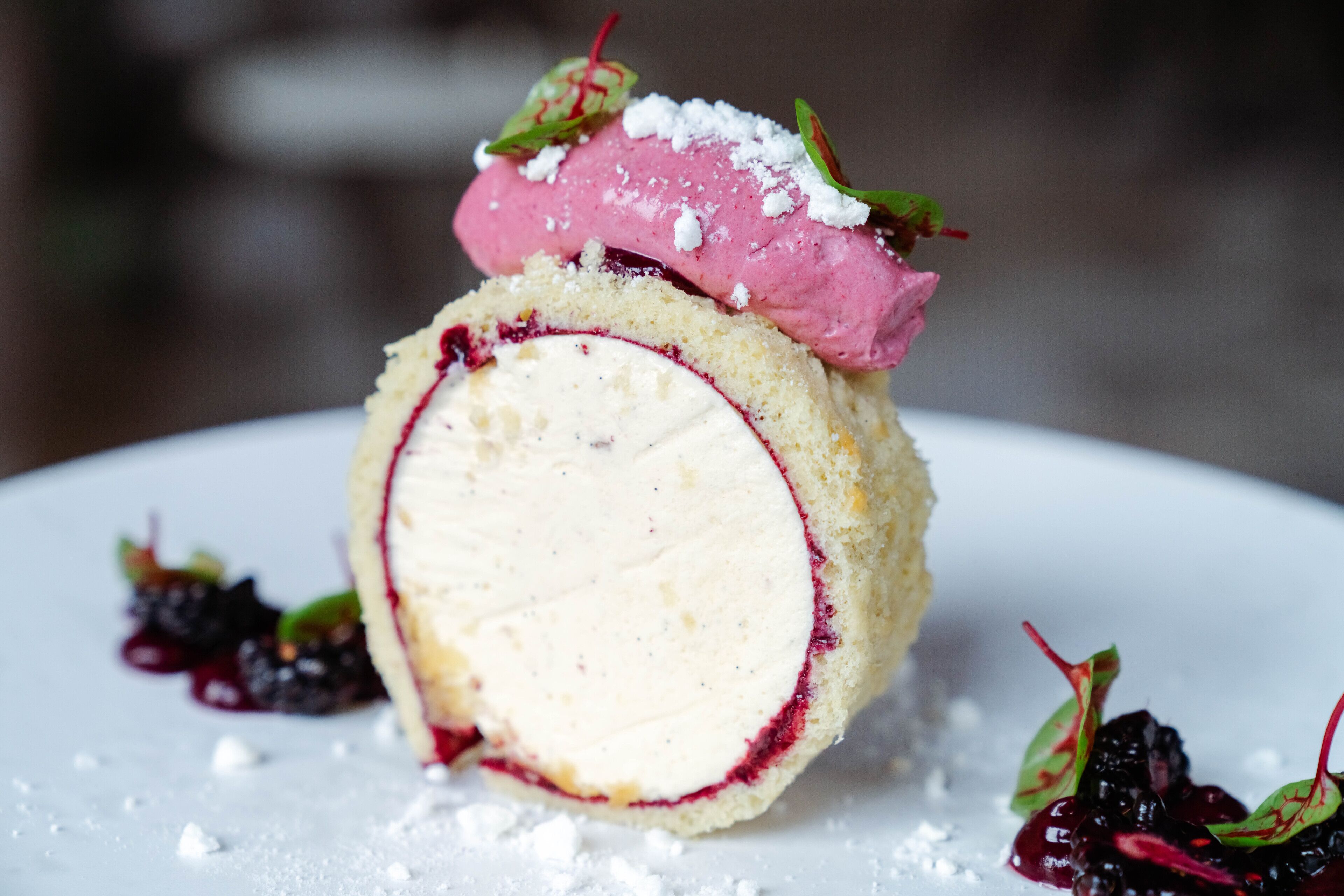 A dessert with a berry filling, topped with a pink scoop and garnished with green leaves and powdered sugar.