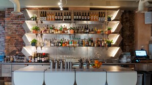 A bar with multiple shelves of bottles and glasses, a modern bar counter, and a digital screen displaying "The Alan".
