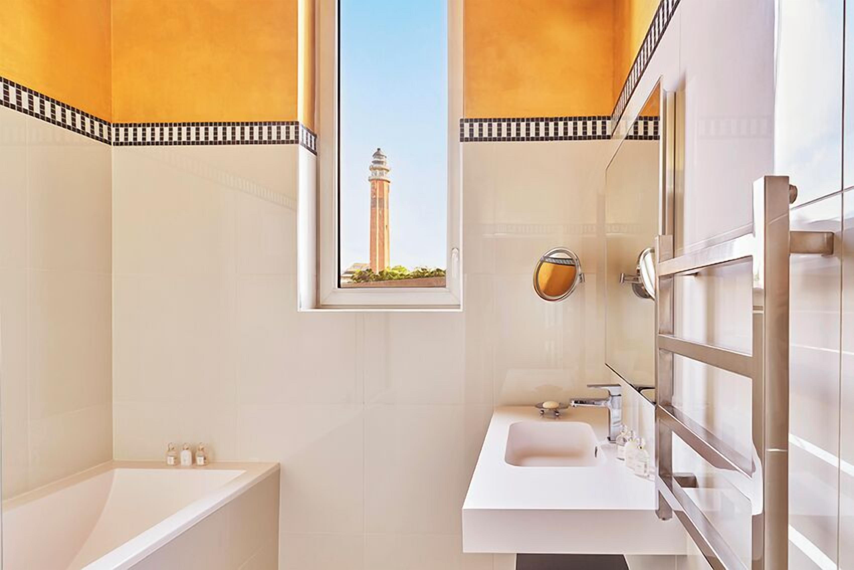 A modern bathroom with a large bathtub, a sink, and a mirror. There is a window with a view of a tower.