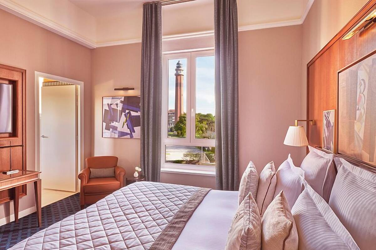 A hotel room with a large bed, a desk, a chair, and a window with a view of a tower.