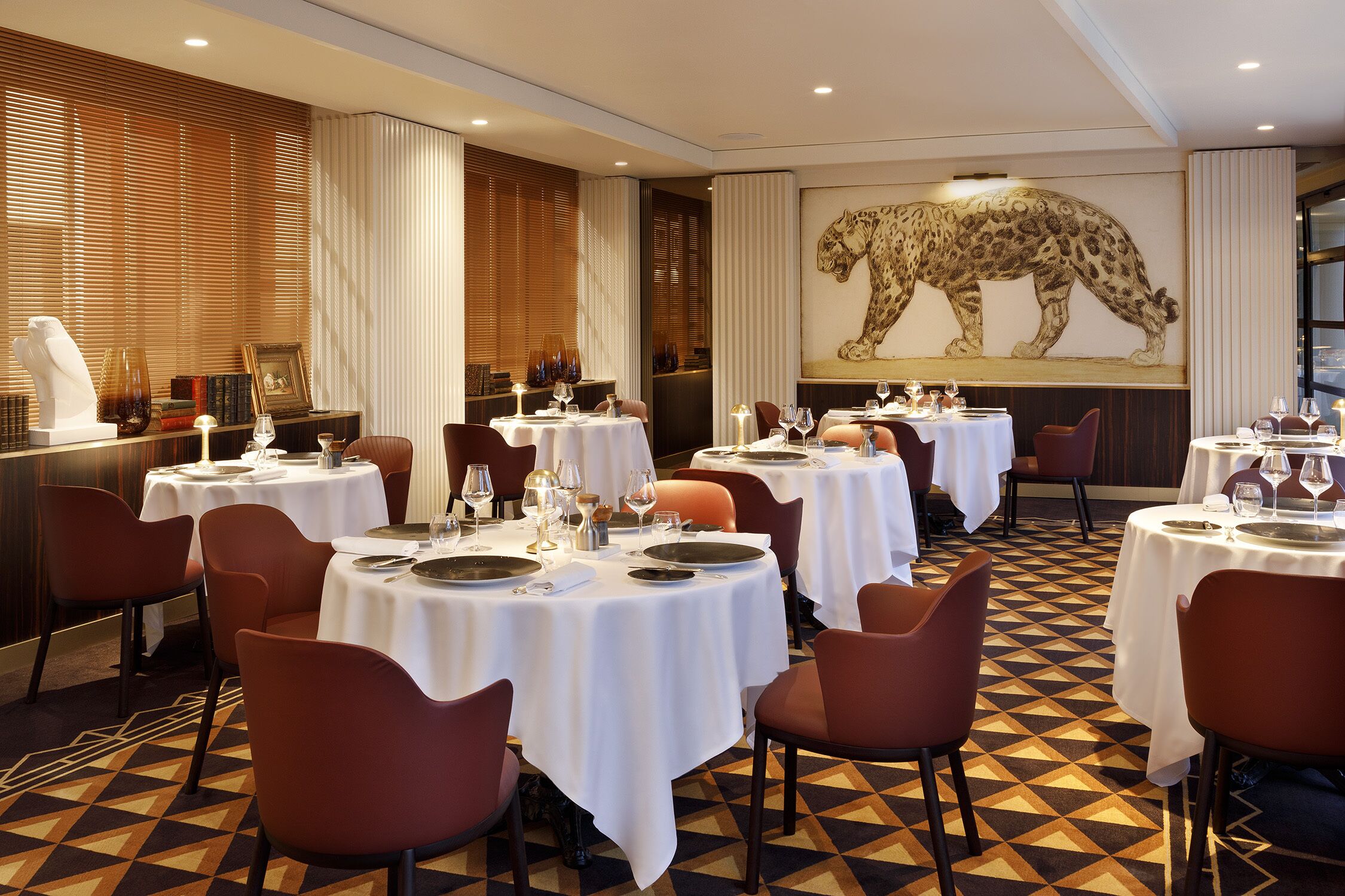 A restaurant with round tables, red chairs, and a leopard mural on the wall.