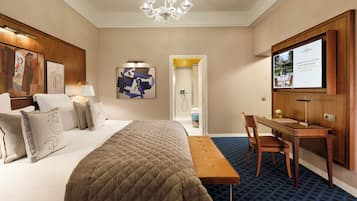 A hotel room with a bed, a desk, a chair, a television, and artwork on the walls.