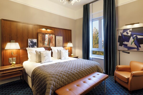 Habitación de hotel con una cama grande, un banco, una silla, un escritorio y una ventana con cortinas.