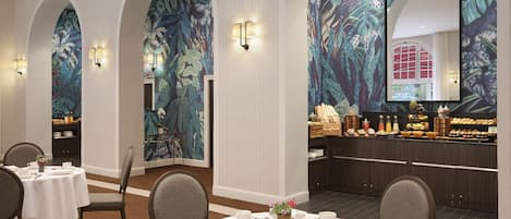 A dining area with round tables set for service, a buffet counter, and a large mirror reflecting the room.