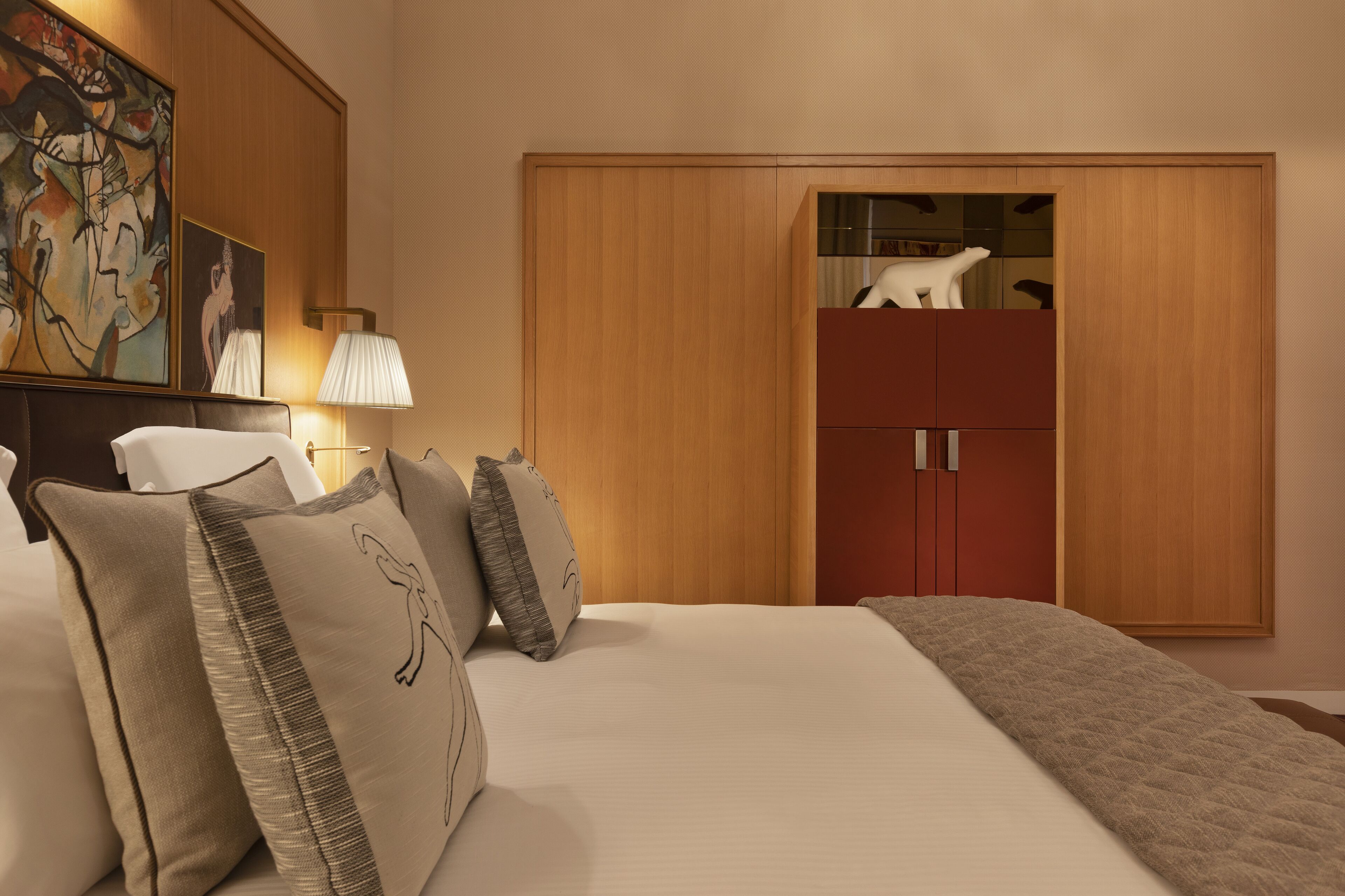 A hotel room with a large bed, a wardrobe, a nightstand with a lamp, and a painting on the wall.
