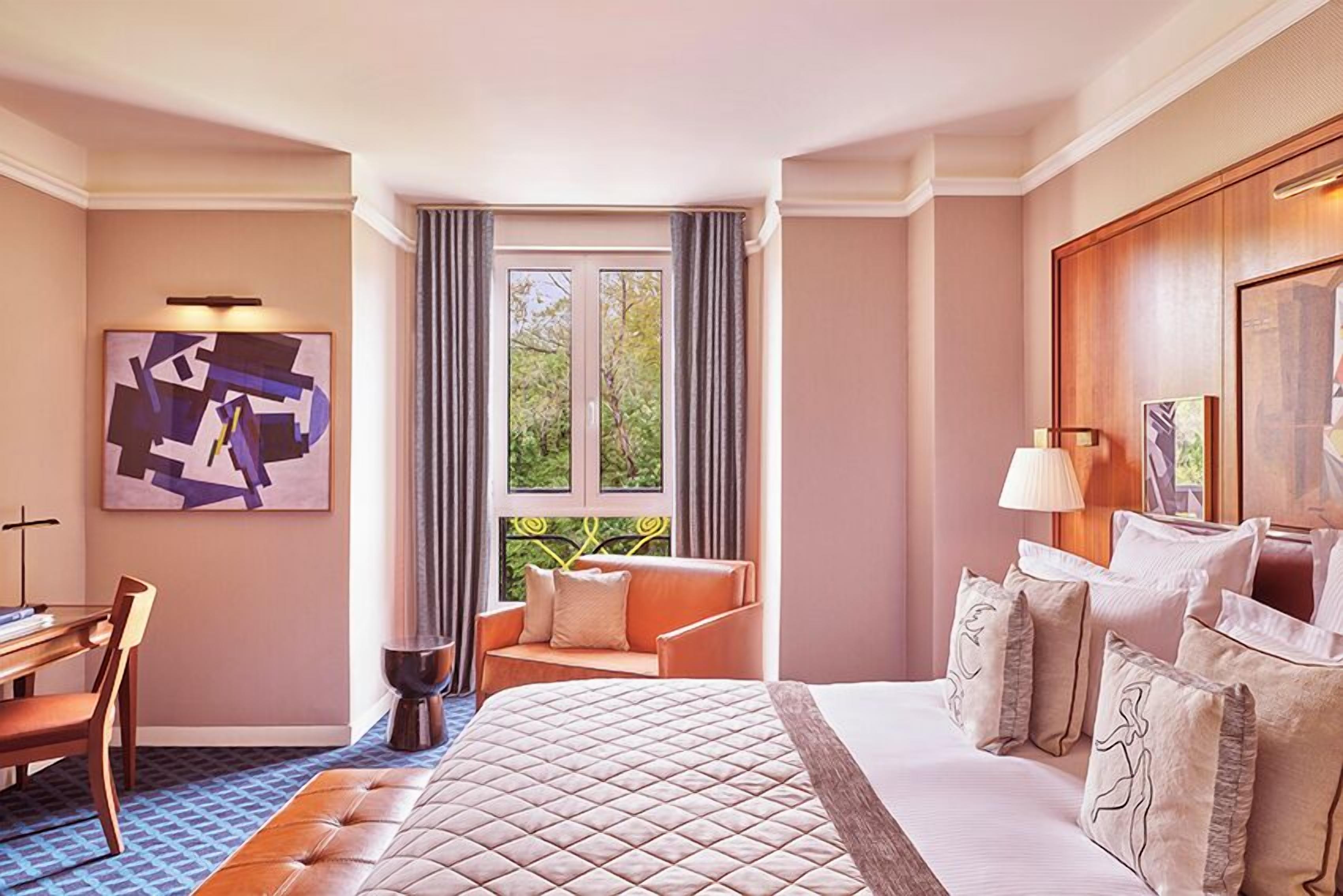 Una habitación de hotel con una cama grande, un escritorio, una silla, una ventana con cortinas y un cuadro en la pared.