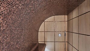 A modern bathroom with a curved brick wall, a wooden bench, and a tiled floor. - Hôtel Barrière Le Westminster Le Touquet (Le Touquet-Paris-Plage)