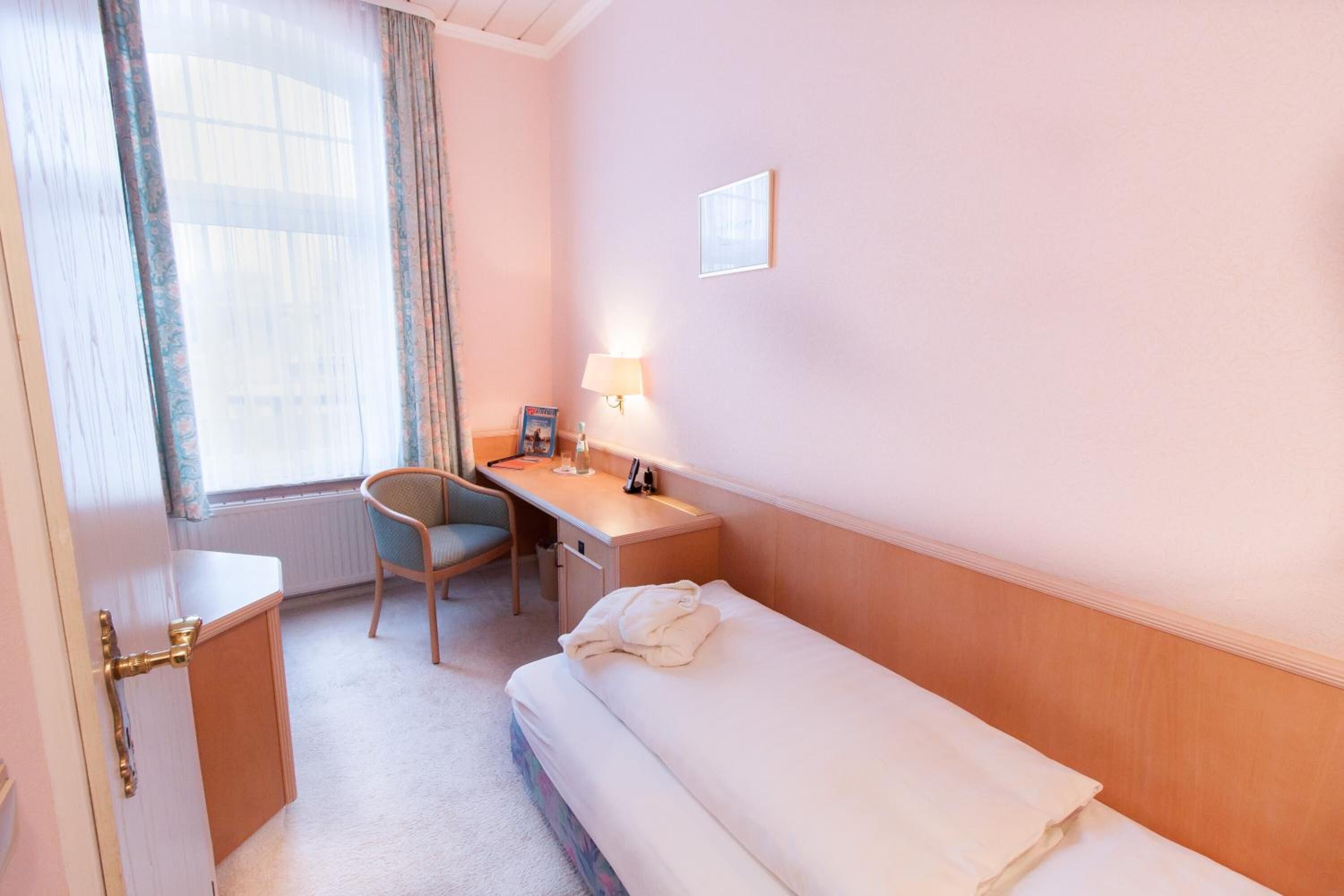 A hotel room with a bed, a desk, a chair, a lamp, and a window with curtains.