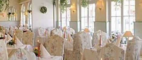 A banquet hall with round tables, floral chairs, and large arched windows.
