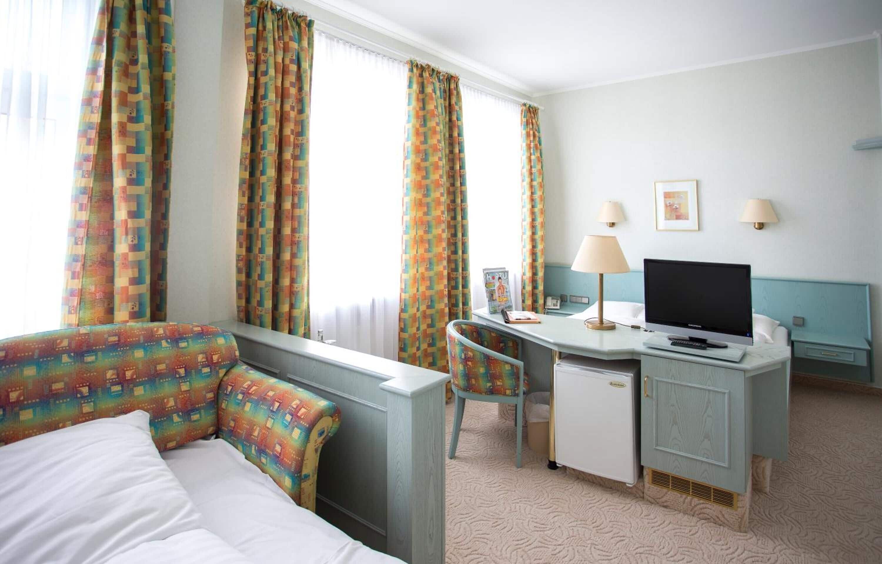 Una habitación de hotel con cama, escritorio, silla, televisor y cortinas.