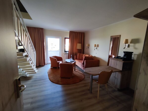 Habitación de hotel con escalera, sofá, mesa de comedor y pequeña cocina.