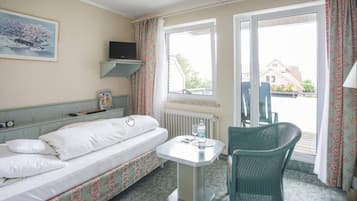 Habitación de hotel con una cama, una mesita pequeña, una silla, un televisor en un estante y una ventana con cortinas.