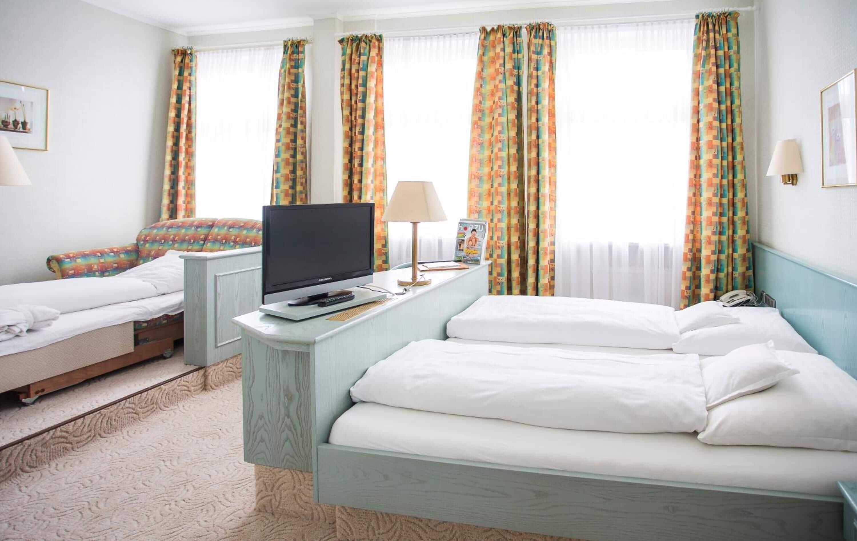 A hotel room with two single beds, a desk with a television, and a magazine.
