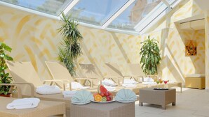 A sunlit room with wicker lounge chairs, a central table with fruit and drinks, and potted plants. - Nordseehotel Freese (Juist)