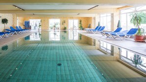 A large indoor swimming pool with blue lounge chairs and potted plants. - Nordseehotel Freese (Juist)