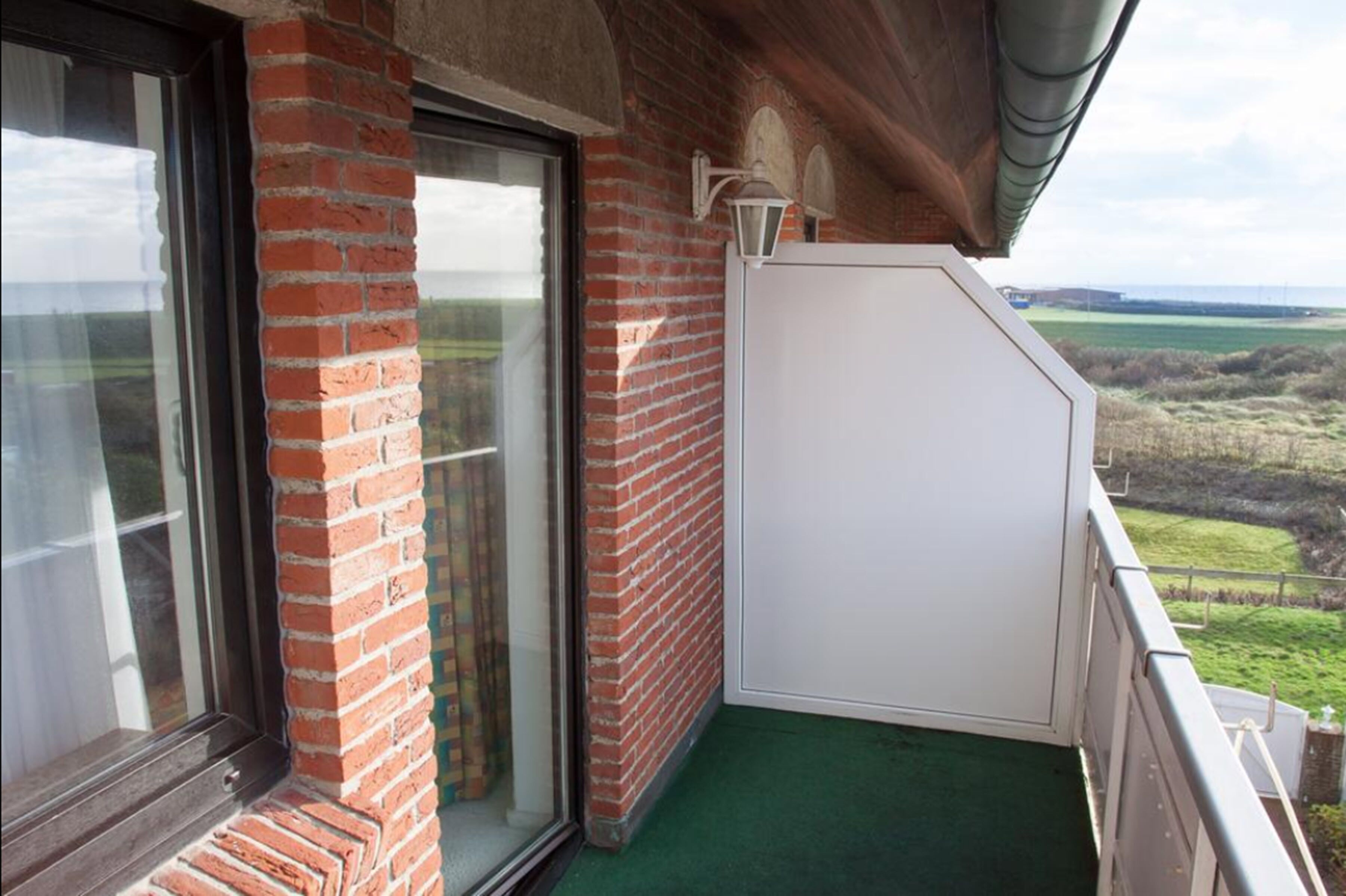Un balcón con un muro de ladrillo, una puerta corredera de vidrio y una puerta blanca.