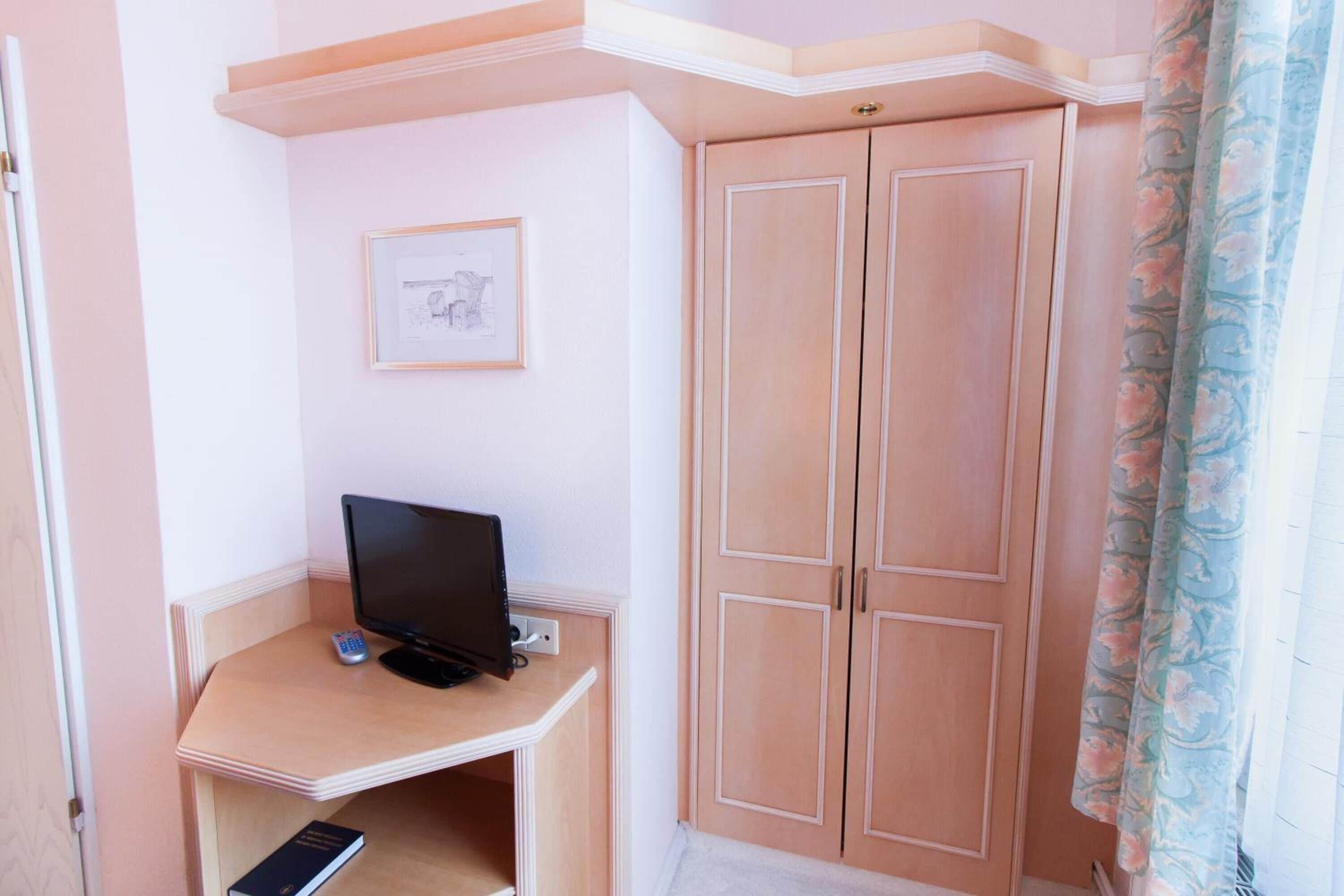 A room with a wooden desk, a television, a wardrobe, and a framed picture on the wall.