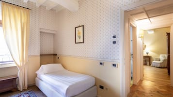 Una habitación de hotel con cama, ventana con cortinas, papel tapiz estampado, un cuadro en la pared y suelo de madera.