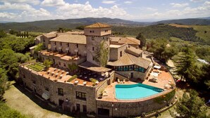 Un edificio histórico de piedra con piscina, jardines en terrazas y vistas a las colinas circundantes.