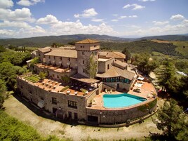 Un edificio histórico de piedra con piscina, jardines en terrazas y vistas a las colinas circundantes.