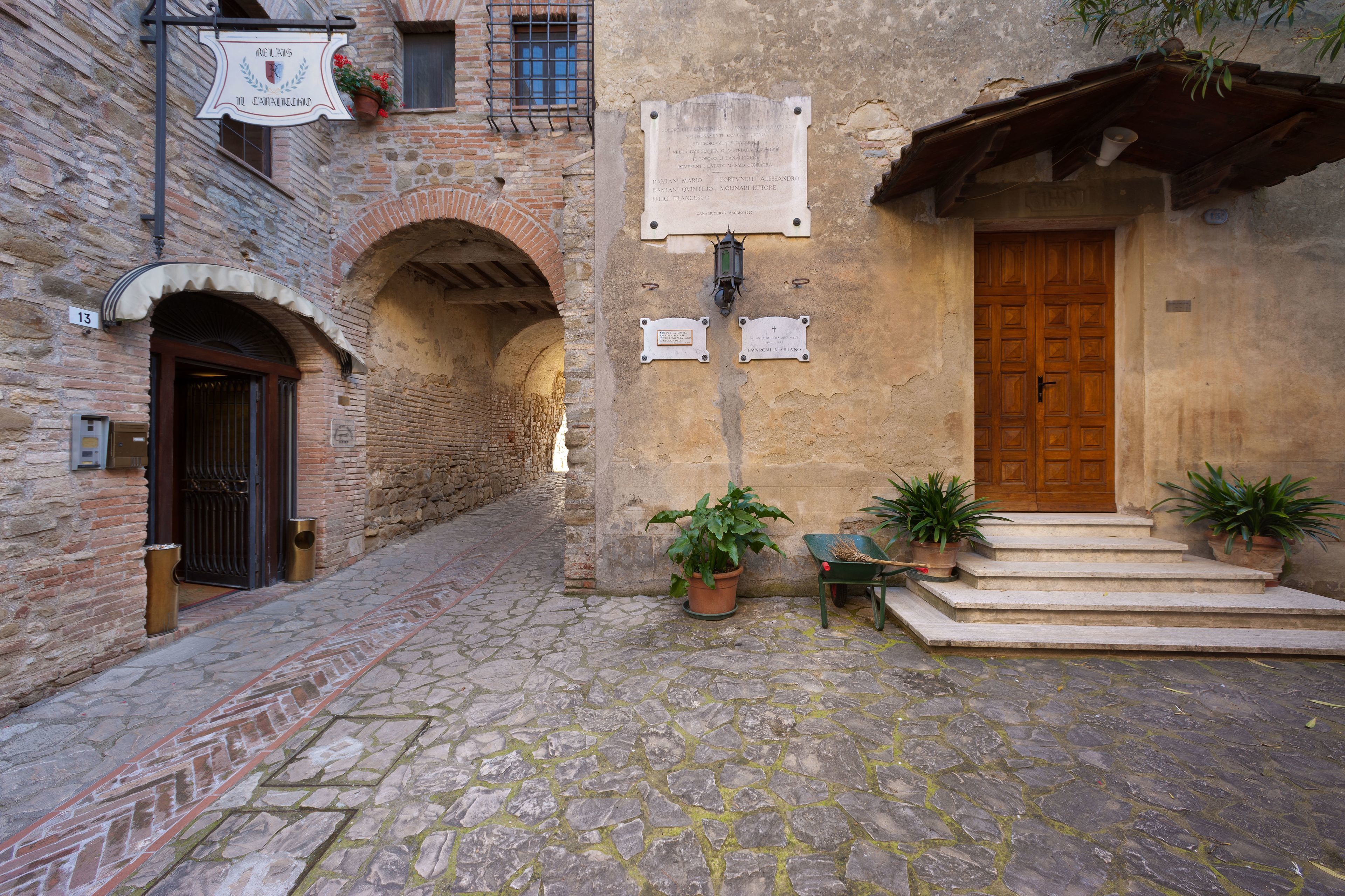 A cobblestone courtyard with a wooden door, potted plants, and stone walls.