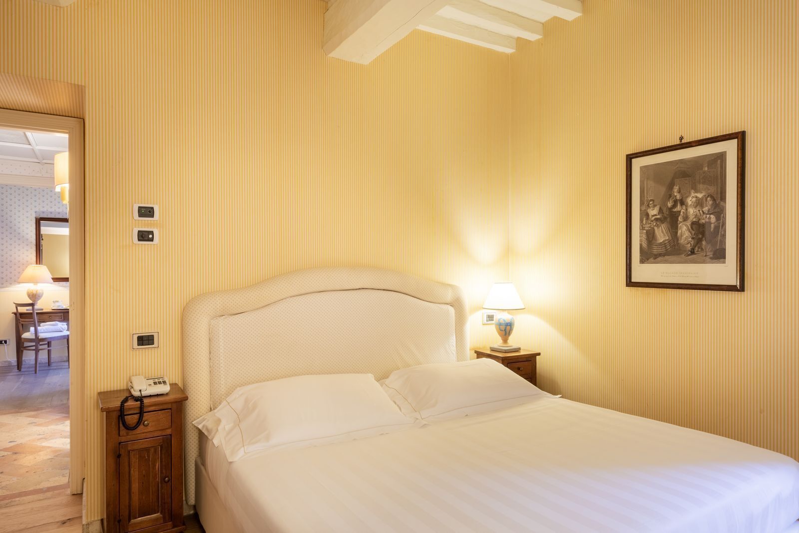 A hotel room with a bed, a nightstand with a lamp, a telephone, and a framed picture on the wall.