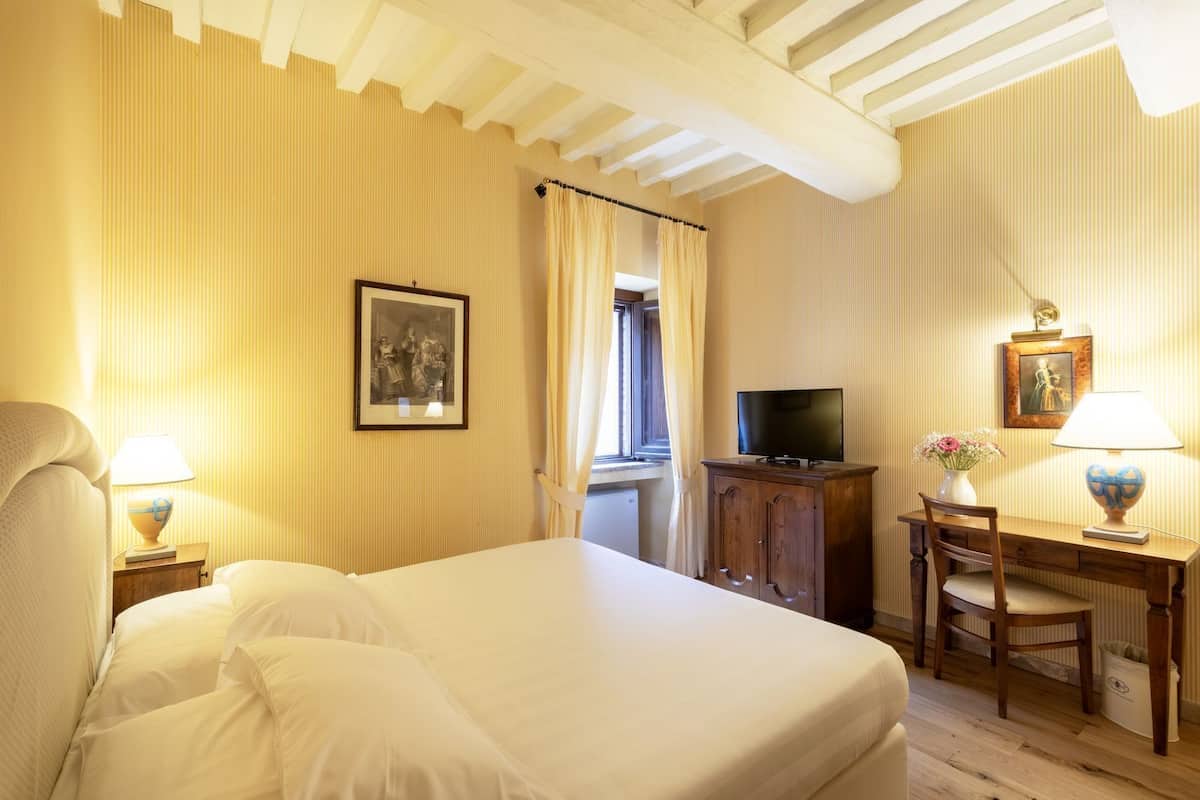A hotel room with a large bed, a desk with a chair, a television, and a framed picture on the wall.