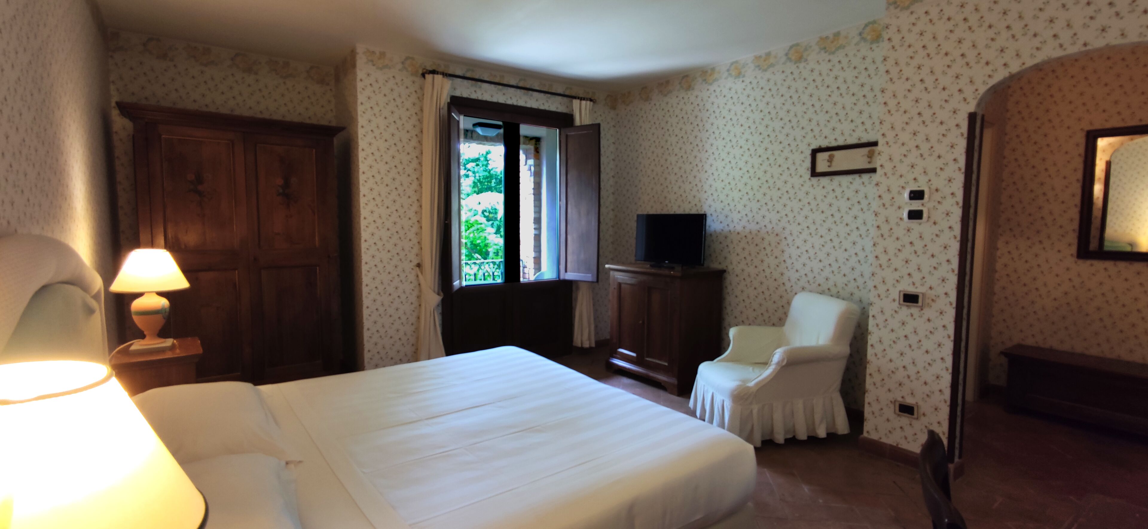 A hotel room with a bed, a chair, a TV, and a wardrobe.