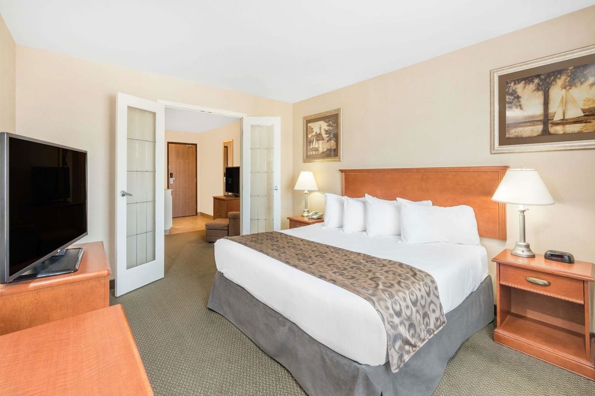 Quarto de hotel com uma cama, abajures, televisão, escrivaninha e uma cadeira.