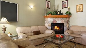Ein Wohnzimmer mit Kamin aus Stein, beigen Sofas, einem Glastisch und einem Beistelltisch mit Lampe.