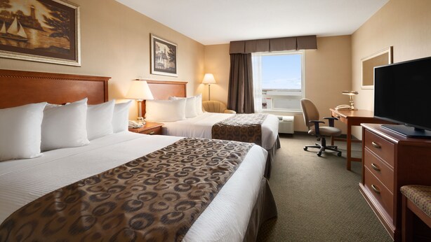 Ein Hotelzimmer mit zwei Betten, einem Schreibtisch, einem Stuhl, einem Fernseher und einem Fenster mit Vorhängen.