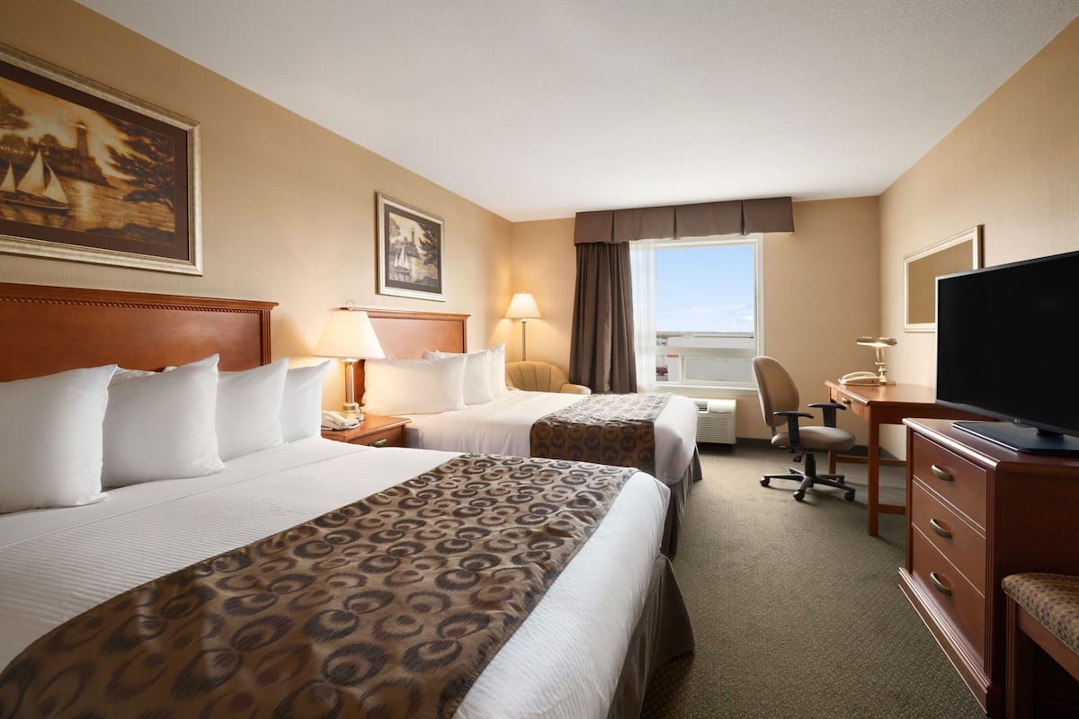 Quarto de hotel com duas camas, uma mesa, uma cadeira, televisão e janela.