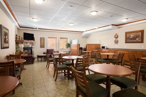 A restaurant with multiple wooden tables and chairs, a stone fireplace, and a television mounted on the wall.
