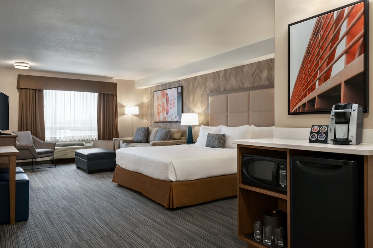 A hotel room with a large bed, a desk, a chair, a TV, a coffee machine, and a microwave.