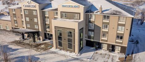 Un hotel de varios pisos con letreros que dicen "CANALTAI" y "WATERSLIDE", que presenta un diseño arquitectónico moderno con grandes ventanales y techo plano.
