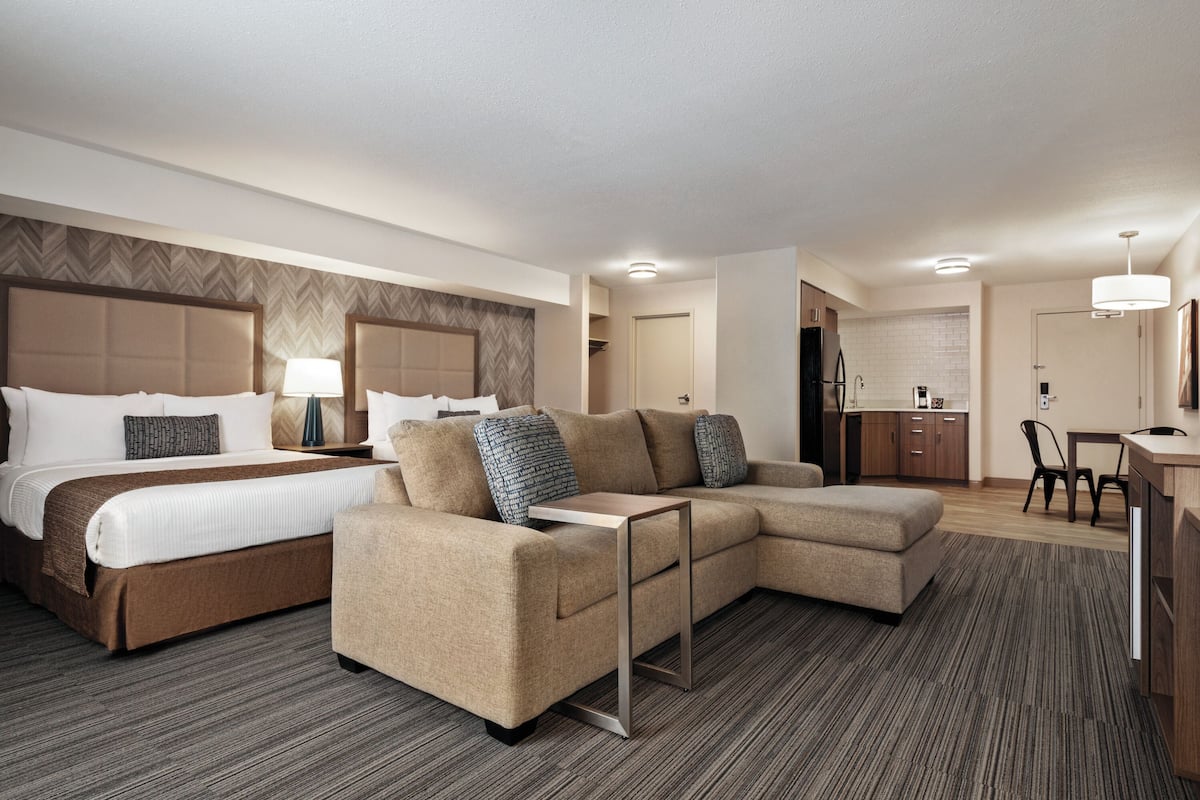 A hotel room with a large bed, a sofa, a desk, and a kitchenette.