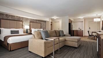 A hotel room with a large bed, a sofa, a desk, and a kitchenette.