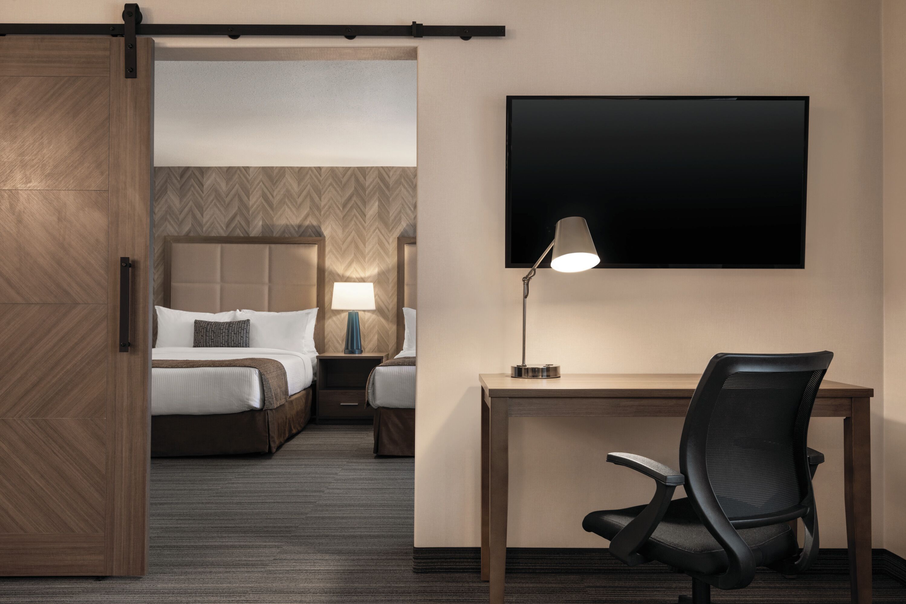 Ein Hotelzimmer mit Bett, Schreibtisch, Stuhl und einem an der Wand befestigten Fernseher.