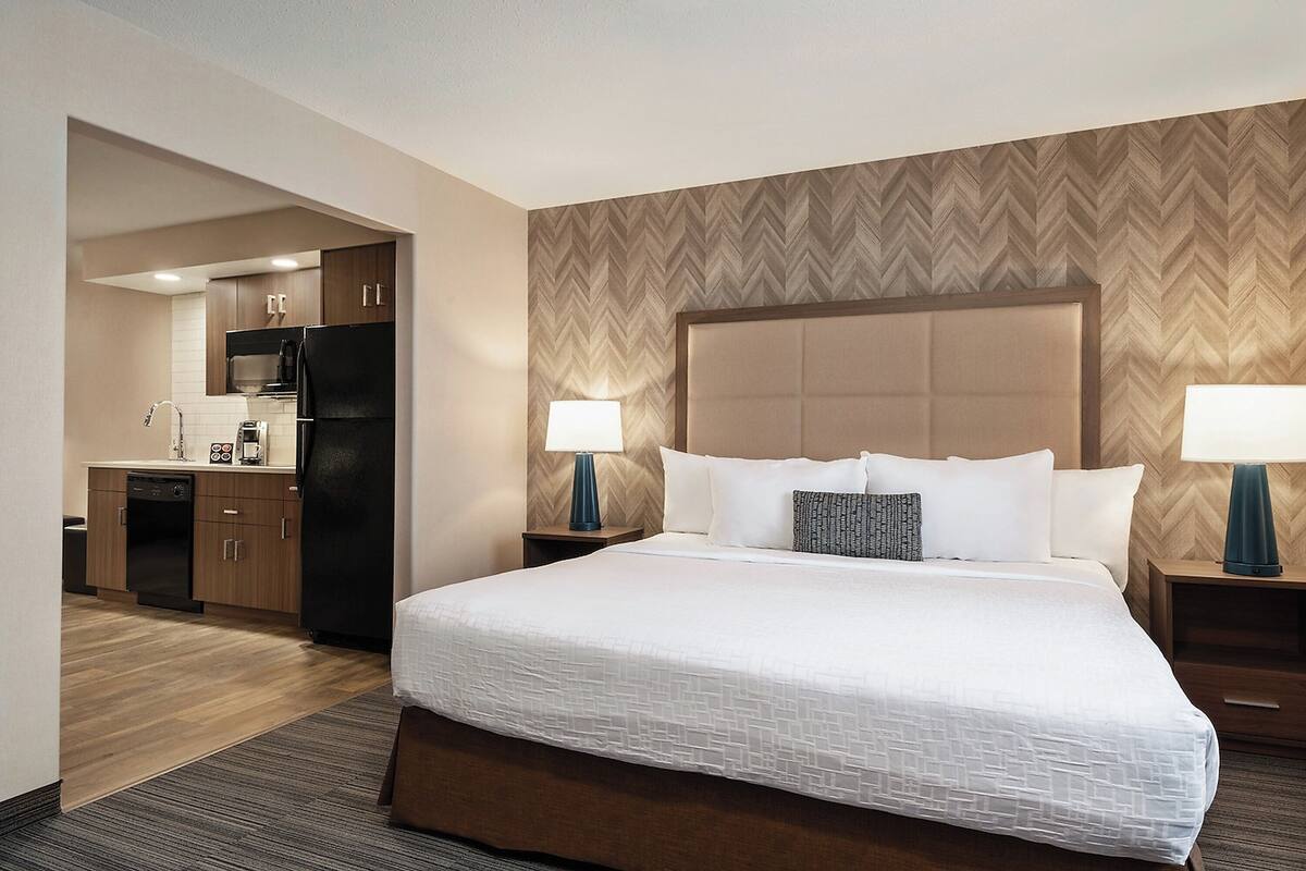 A hotel room with a large bed, a separate kitchenette, and a herringbone-patterned wall.