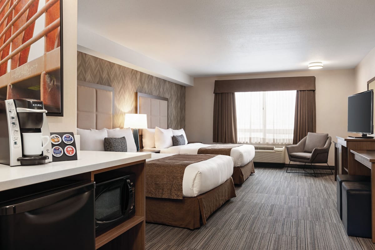 A hotel room with two beds, a desk with a coffee maker, a TV, and a microwave.