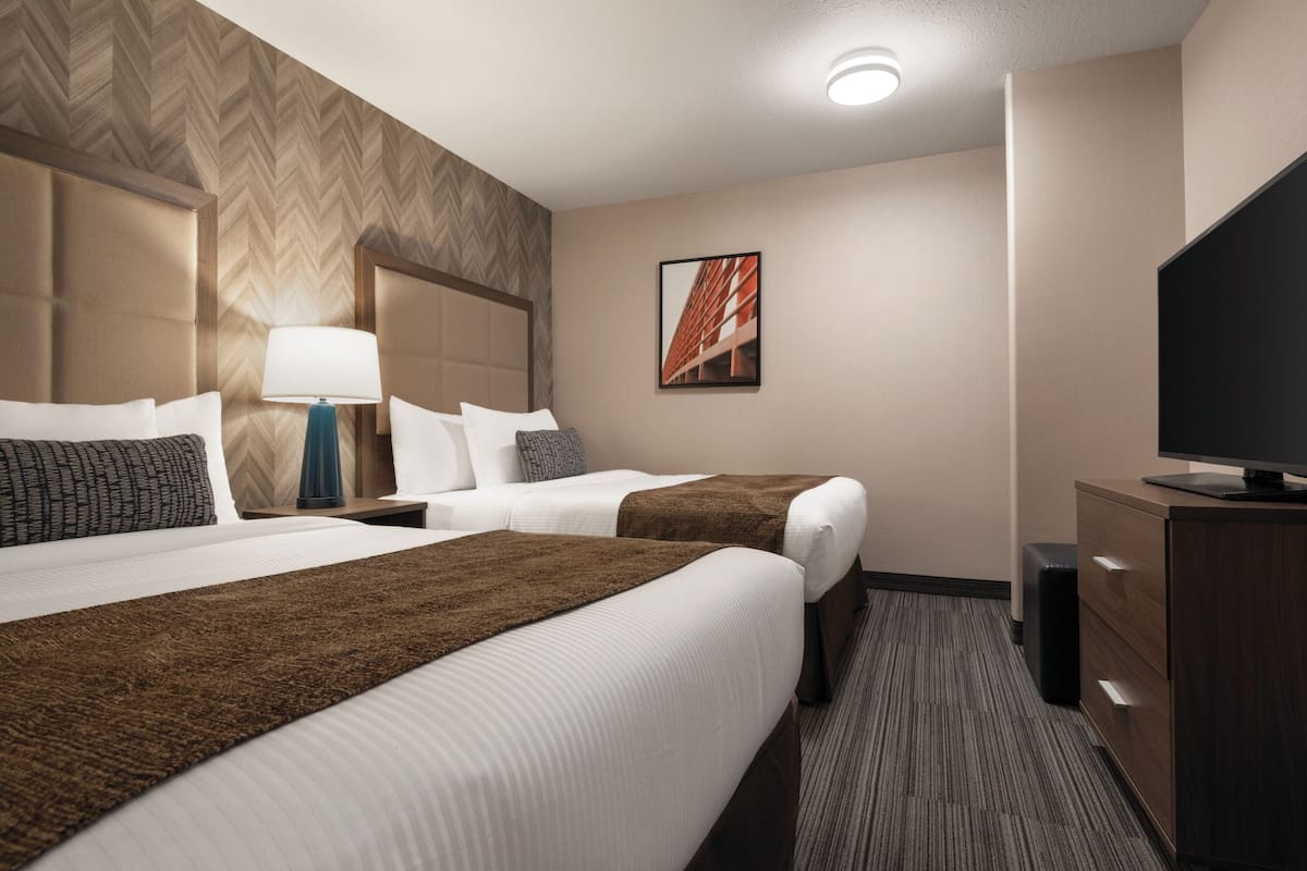 A hotel room with two beds, a television, a desk, and a wall-mounted picture.