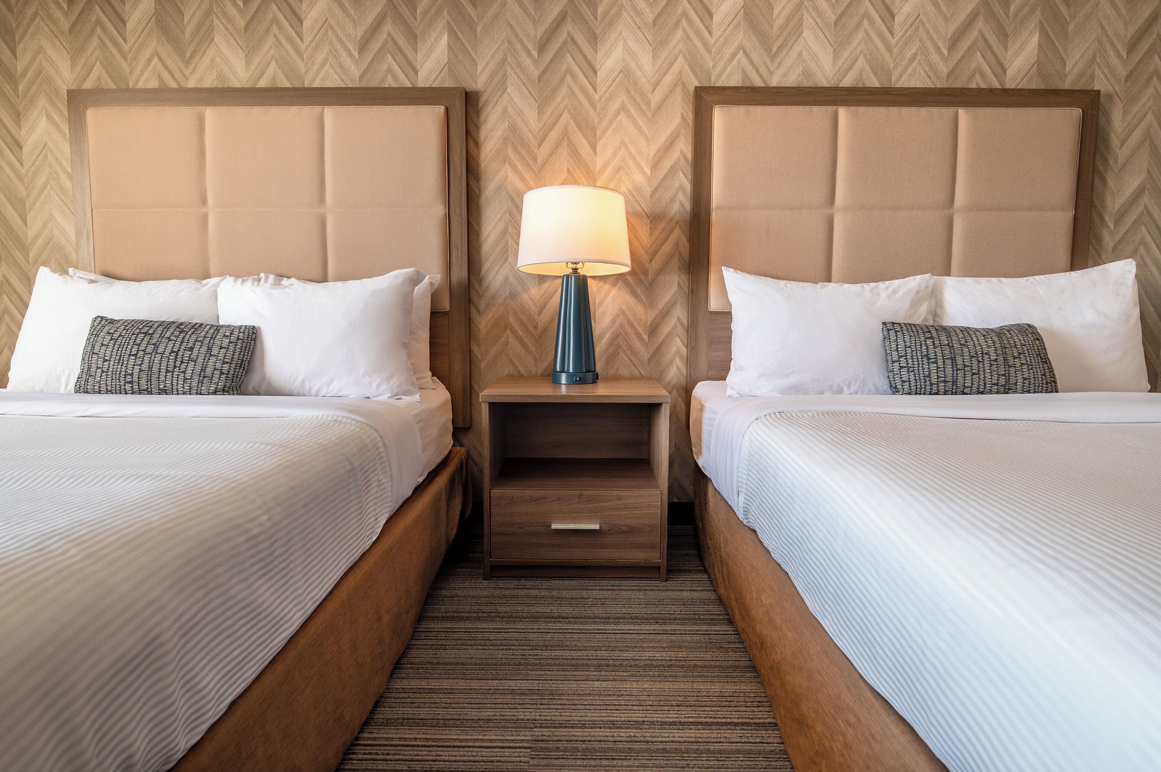 Une chambre d’hôtel avec deux lits, une table de chevet avec une lampe et un mur orné d’un motif en chevrons.