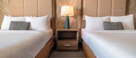 Een hotelkamer met twee bedden, een nachtkastje met een lamp en een wand met een herringbone patroon.